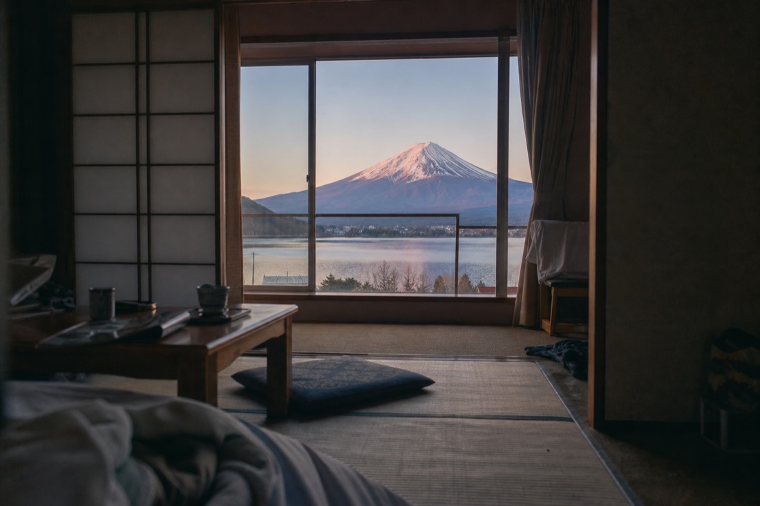 A tatami room at dawn with the window open onto a still lake and the snow-capped cone of Mount Fuji
