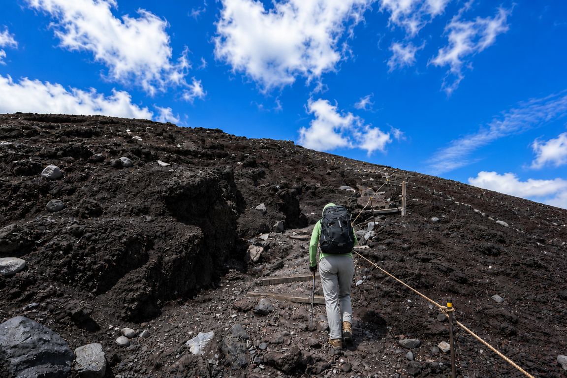 Adventurer hiking up the Fujinomiya Trail on Mount Fuji surrounded by lava rocks during a Mt. Fuji Tours experience with our agency
